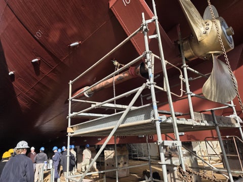 Students walking under the hull of R/V Sally Ride with scaffolding and the rudder.