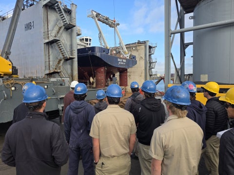 Students wearing hardhats and looking at R/V Sally Ride with their backs to the camera.