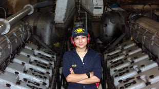 Cadet Lotus Garica standiCadet Lotus Garcia standing between the engines aboard the Training Ship Golden Bear during Summer Sea Term.