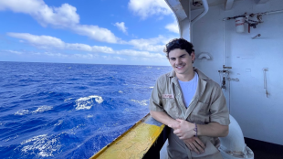Cadet Elijah Kadish standing on a side deck of Training Ship Golden Bear looking out at the ocean.