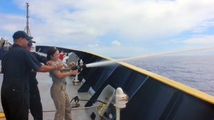 Cadet Gia Espejo using a water canon on the deck of Training Ship Golden Bear.