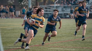 Zion Jerge carrying a rugby ball down the pitch with other players in pursuit.
