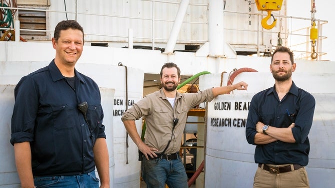 Three individuals pose for photo next to their research project